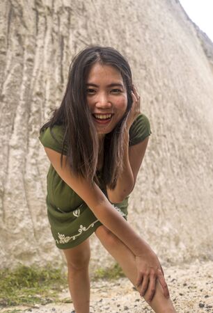 natural portrait of young beautiful and happy Asian Korean woman in green Summer dress  posing playful at rocky mountain smiling cheerful enjoying outdoors and having funの写真素材