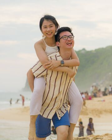 sweet and romantic lifestyle portrait of young happy Asian Chinese couple in love enjoying holiday on beautiful beach walking together by the sea playful and affectionate in relationship conceptの写真素材