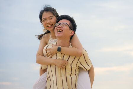 sweet and romantic lifestyle portrait of young happy Asian Korean couple in love enjoying holiday or weekend with man carrying girlfriend on his back cuddling and playing togetherの写真素材