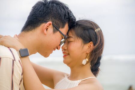sweet and romantic lifestyle portrait of young happy Asian Chinese couple in love enjoying holiday on beautiful beach walking together by the sea playful and affectionate in relationship conceptの写真素材