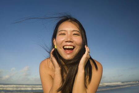 natural lifestyle portrait of young attractive and happy Asian Japanese woman in swimsuit walking on...
