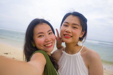 young beautiful and happy couple of attractive Asian Korean women at the beach enjoying holidays having fun taking selfie together with mobile phone in girls friendship conceptの写真素材