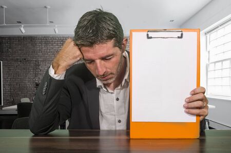 depressed and worried businessman holding clipboard with copy space reporting company financial crisis and problems feeling concerned and frustrated in corporate work difficultiesの写真素材