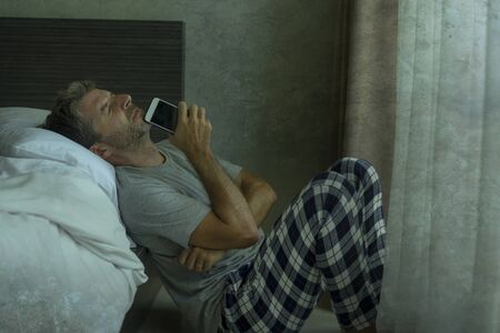 dramatic indoors portrait of mid adult man crying sad and depressed at bedroom floor with mobile...
