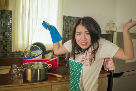cook and wash overwork - young tired and stressed Asian Chinese woman in kitchen apron working at home exhausted and desperate complaining frustrated and overwhelmedの写真素材