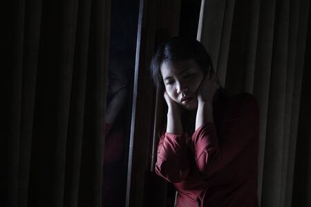 dark dramatic portrait of young beautiful scared and depressed Asian   woman feeling overwhelmed and in panic lockdown alone at home during covid-19 virus outbreak quarantineの写真素材