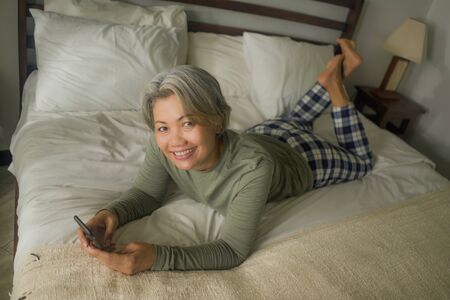 home lifestyle portrait of attractive and happy middle aged woman on her 50s using internet mobile phone in bed relaxed and cheerful online dating or enjoying social media appの写真素材