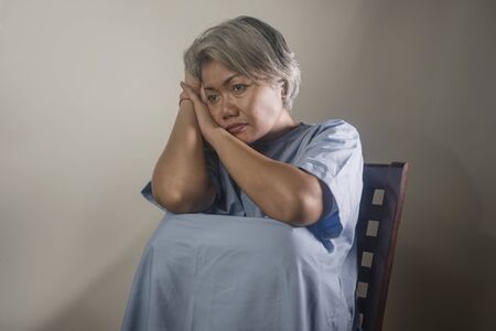 dramatic portrait of attractive sad and depressed mature woman with grey hair in pain suffering mental disorder or depression problem wearing patient gown feeling sick and abandonedの写真素材