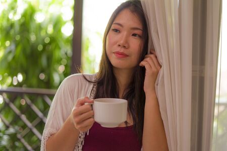 lifestyle portrait of young happy and beautiful Asian Chinese woman having morning coffee or tea at...