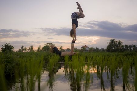 outdoors sunset acroyoga workout silhouette- young happy and fit couple practicing acro yoga drill at beautiful rice field enjoying nature and healthy lifestyle doing acrobatic poseの写真素材