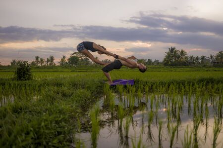 outdoors sunset acroyoga workout silhouette- young happy and fit couple practicing acro yoga drill...
