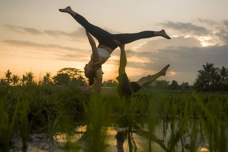 outdoors sunset acroyoga workout - young happy and fit couple practicing acro yoga drill at beautiful rice field enjoying nature and healthy lifestyle doing acrobatic poseの写真素材