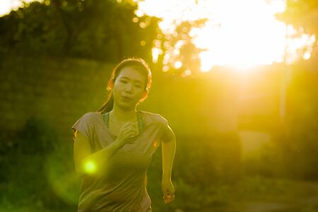 outdoors running workout - young happy and dedicated Asian Korean woman jogging at beautiful city park or countryside trail on sunset enjoying fitness and cardio activity in healthy lifestyleの写真素材