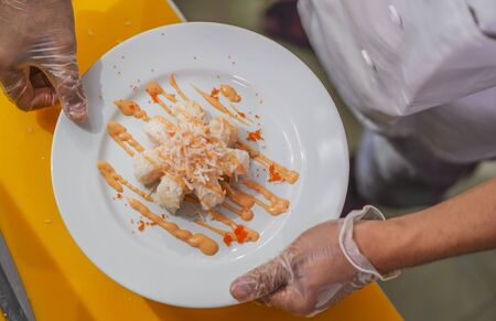 hands in gloves of Asian professional chef preparing delicious and healthy Japanese sushi rolls at...