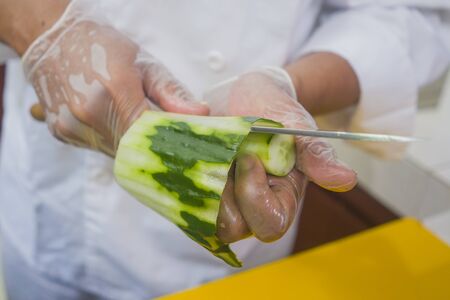 hands in gloves of Asian professional chef preparing Japanese sushi rolls cutting cucumber with knife at home or restaurant kitchen making traditional Japan foodの写真素材