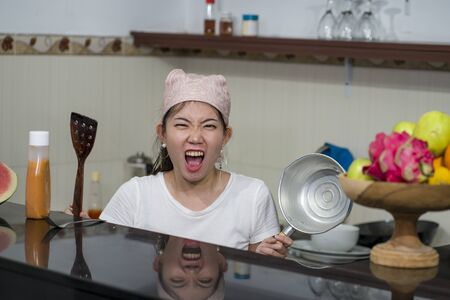 lifestyle home portrait of beautiful overwhelmed and stressed Korean girl working in kitchen unhappy and upset housekeeping - young frustrated Asian woman screaming in domestic chores stressの写真素材