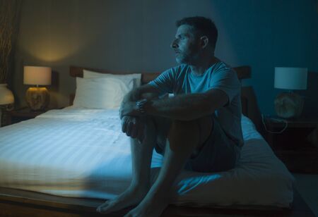 dramatic portrait in the dark of attractive depressed and worried man on bed suffering depression...
