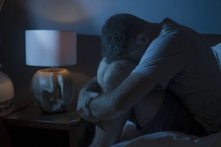 dramatic portrait in the dark of attractive depressed and worried man on bed suffering depression crisis and anxiety feeling lost sitting sleepless in insomnia and life problem conceptの写真素材
