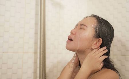 home lifestyle portrait of young beautiful and happy Asian Korean woman taking a shower in the...