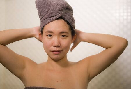 home lifestyle portrait of young beautiful and happy Asian Chinese woman with head wrapped in towel...