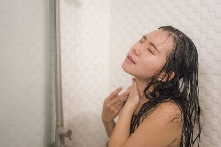 home lifestyle portrait of young beautiful and happy Asian Chinese woman taking a shower in the...