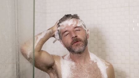 morning shower - lifestyle portrait of young attractive and happy man with beard taking a shower at home washing his hair with shampoo enjoying cheerful in wellness and hygiene conceptの写真素材