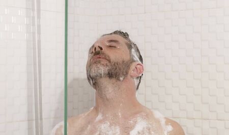 morning shower - lifestyle portrait of young attractive and happy man with beard taking a shower at...