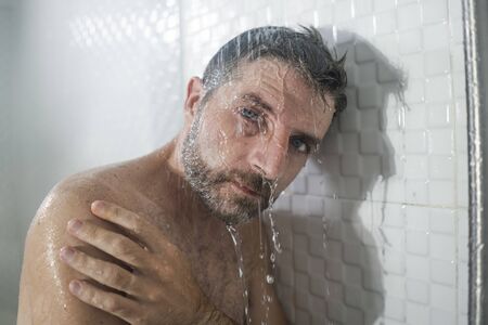 home bathroom dramatic portrait of young attractive sad and depressed man in the shower leaning...
