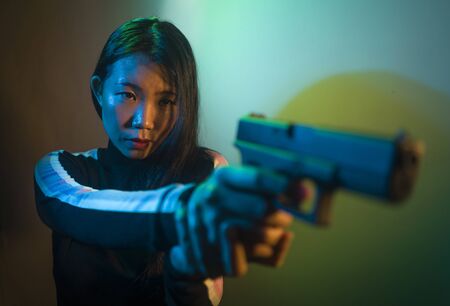 edgy cinematic portrait of young attractive and dangerous special agent woman or Asian mobster girl holding handgun pointing the gun fierce in Hollywood movie styleの写真素材
