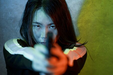 edgy cinematic portrait of young attractive and dangerous special agent woman or Asian mobster girl holding handgun pointing the gun fierce in Hollywood movie styleの写真素材
