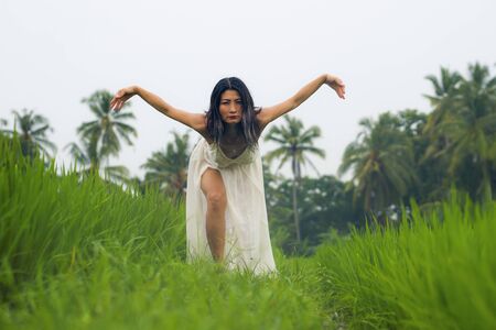 mind and body connection with nature - middle aged attractive and happy Asian Chinese woman in Summer dress enjoying idyllic tropical travel destination dancing feeling freeの写真素材