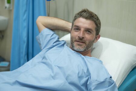 positive and hopeful hospital patient smiling before adversity - young attractive and trustful man lying on clinic bed responding to treatment and healing feeling relaxedの写真素材