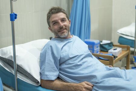 positive and hopeful hospital patient smiling before adversity - young attractive and trustful man lying on clinic bed responding to treatment and healing feeling relaxedの写真素材