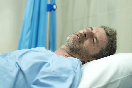 scared and worried man in pain at hospital room - attractive injured man lying on bed suffering painful problem feeling sick and stressed after suffering accident or serious disease の写真素材