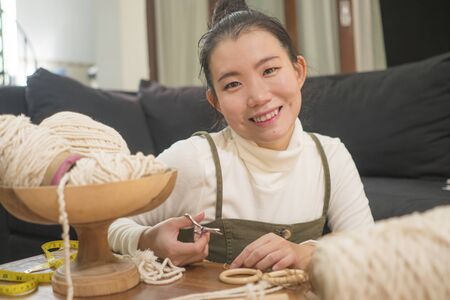 Asian girl enjoying macrame handcraft hobby - young happy and pretty Chinese at home doing macram using ropes, cords and threads in domestic handmade decorationの写真素材