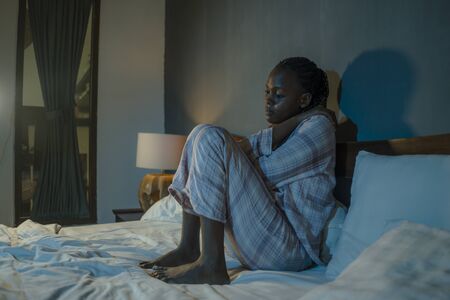young sad and depressed black African  woman sitting on bed at home sleepless and worried at night feeling overwhelmed suffering depression problem and insomniaの写真素材
