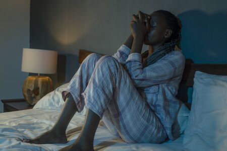 young sad and depressed black afro  woman on bed at home unhappy and sleepless at night feeling overwhelmed suffering depression problem and insomniaの写真素材