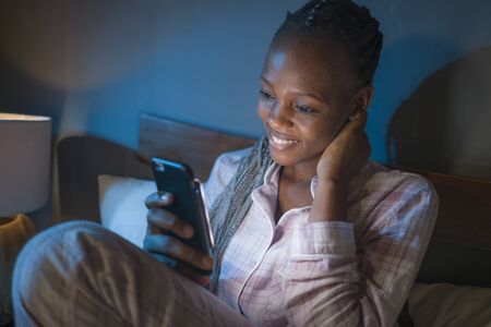 happy African American millennial woman as social media addict - night lifestyle portrait of young...