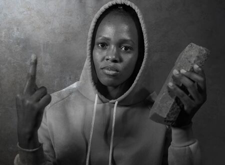 USA anti racist riots - young furious and angry black afro American woman in mask and hoodie shooting brick during street riot against race discrimination demonstration as human rights activistの写真素材