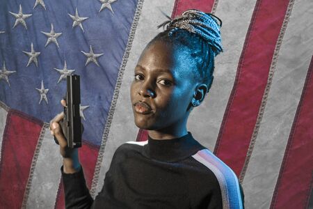 Hollywood movie style portrait of young attractive and confident black African  woman holding gun as...