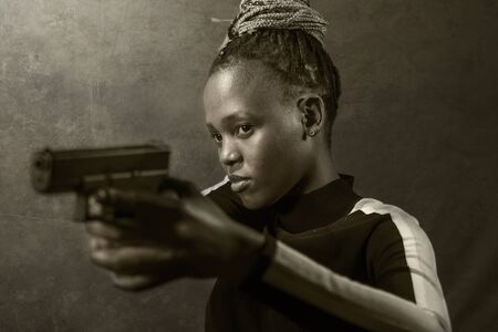 Hollywood movie style portrait of young attractive and confident black African  woman holding gun as...