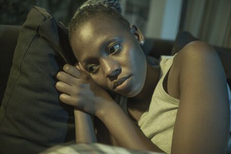 young African American woman suffering depression - sad and depressed black teenager girl in pain at home sofa couch feeling overwhelmed and emotional crying lonely in the darkの写真素材