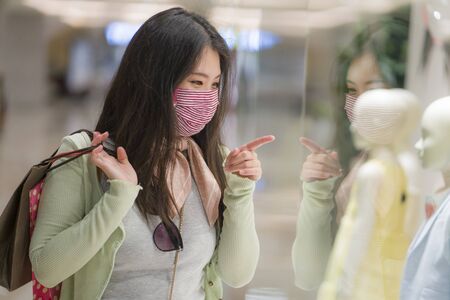 happy Asian at shopping mall in new normal lifestyle - young attractive and beautiful Korean woman with face mask holding shopping bags at fashion center excited enjoying salesの写真素材
