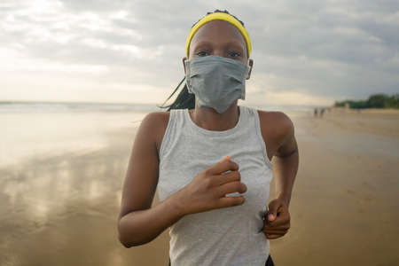 post quarantine runner girl enjoying outdoors workout - young attractive and fit black African American woman running wearing face mask in new normal sport practice concept and healthy lifestyleの写真素材