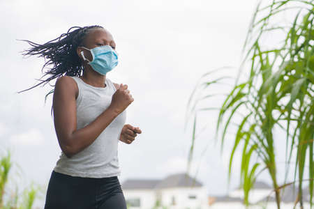 post quarantine runner girl enjoying outdoors workout - young attractive and fit black African American woman running wearing face mask in new normal sport practice concept and healthy lifestyleの写真素材