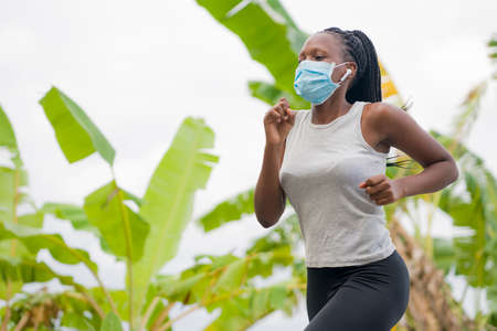 post quarantine runner girl enjoying outdoors workout - young attractive and fit black African American woman running wearing face mask in new normal sport practice concept and healthy lifestyleの写真素材