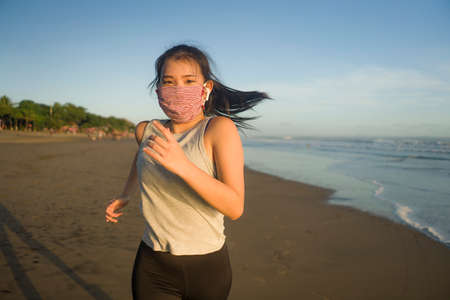 new normal running workout of Asian girl in face mask - young happy and beautiful  woman jogging on...