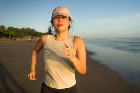 Asian girl running on the beach - young attractive and happy Korean woman doing jogging workout at...