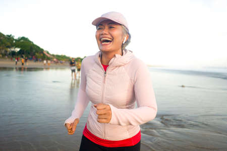 fit and happy middle aged woman running on the beach - 40s or 50s attractive mature lady with grey...