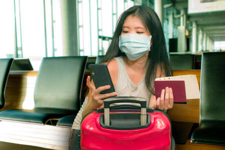 young beautiful and happy Asian Korean tourist woman holding suitcase smiling cheerful and excited waiting at airport terminal departures in holidays travel conceptの写真素材